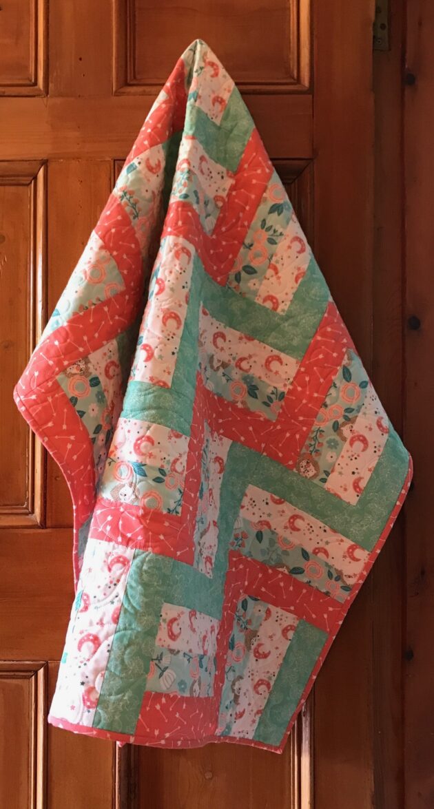 Colourful baby quilt made with the rail fence pattern and quilted with a swirling feather design