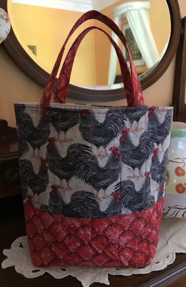 Quilted tote bag with packed roosters on upper half and coordinating red patterned fabric on the lower half