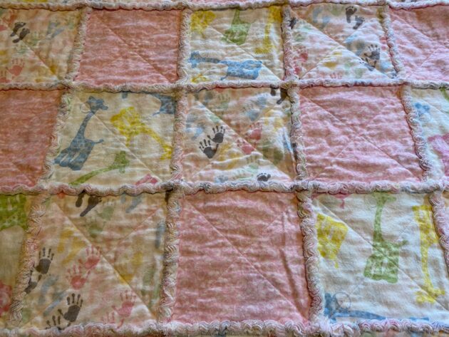 close up view of a a baby rag quilt with colourful baby giraffes, hands and feet