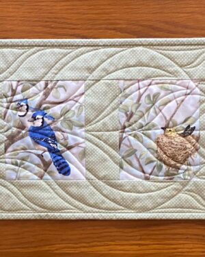 a quilted table runner with six images of birds in trees