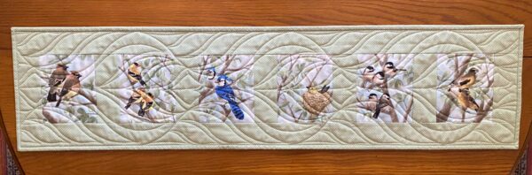 a quilted table runner with six images of birds in trees