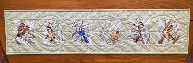 a quilted table runner with six images of birds in trees