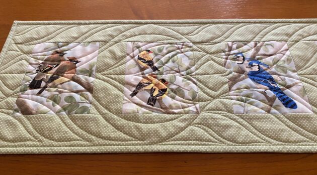 a quilted table runner with six images of birds in trees