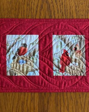 Quilted table runner with six images of birds in trees made with red background fabric