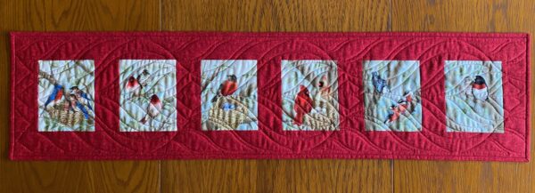 Quilted table runner with six images of birds in trees made with red background fabric