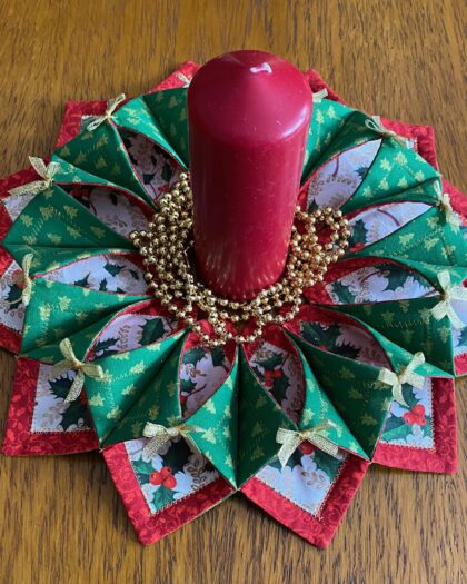 Small fabric Christmas wreath with miniature gold metallic Christmas trees on green fabric on the back which wraps around to the front and fixed with gold metallic bows, holly leaf fabric trimmed in red on the front.