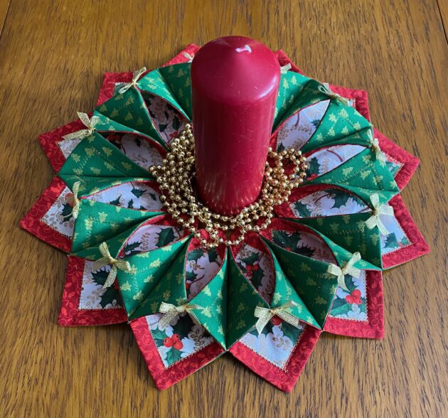 Small fabric Christmas wreath with miniature gold metallic Christmas trees on green fabric on the back which wraps around to the front and fixed with gold metallic bows, holly leaf fabric trimmed in red on the front.