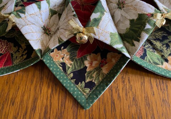 detailed view of a Christmas Poinsettia fabric wreath showing one of the sections with a gold metallic bow and jingle bell