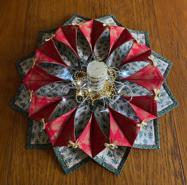 A candle, gold beads and LED lights are placed in the centre of a large fabric Christmas table wreath made with green, red and white cotton fabrics