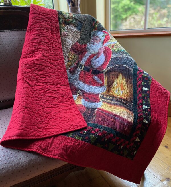 A Christmas throw quilt featuring Santa Claus checking his list thrown over a seat