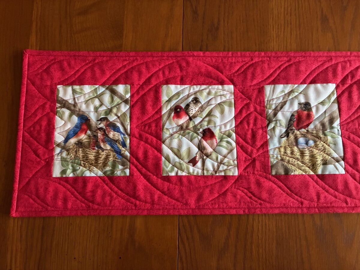 partial view of a quilted table runner in Christmas red showing three lovely images of birds