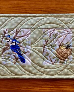cotton quilted table runner with six colourful images of birds on a sage green background with white pin dots