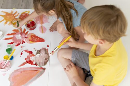 two young children sitting at a table painting pictures
