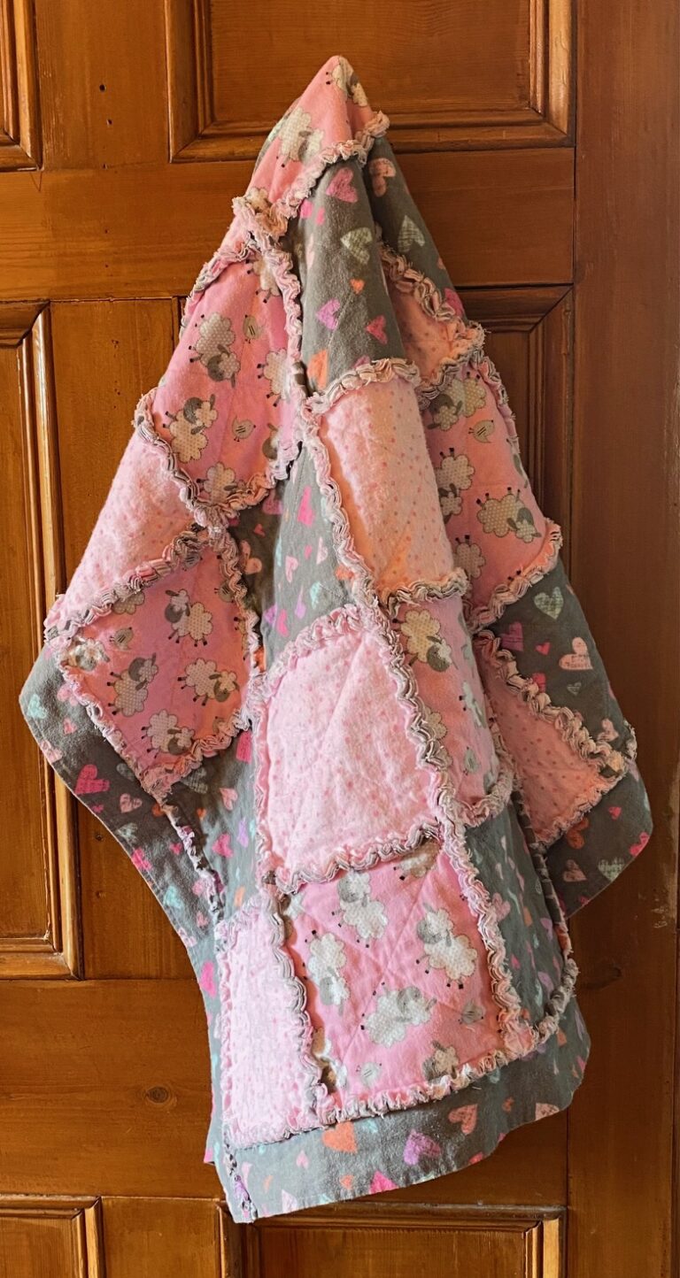 a lovely pink and grey cotton flannel baby rag quilt hanging on a door