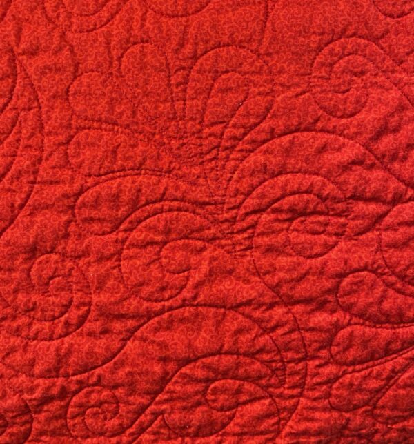 A photo of the red backing on a floral throw quilt showing the feathery quilting design done in red thread