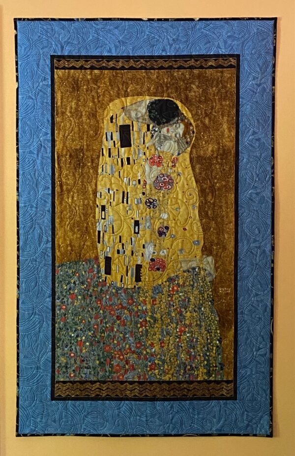 A quilted wall hanging of Klimt's "The Kiss" with a blue border