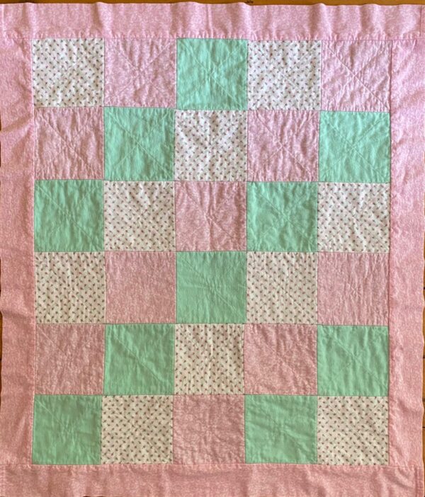 The back side of a pink, green and white baby rag quilt made with cotton flannel