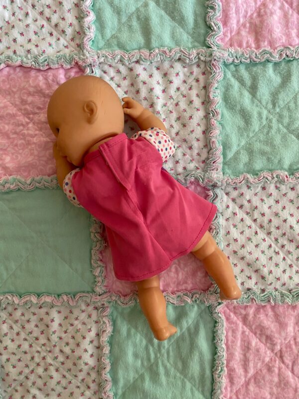 A close-up view of a pink green and white flannel baby quilt with a baby doll lying on top
