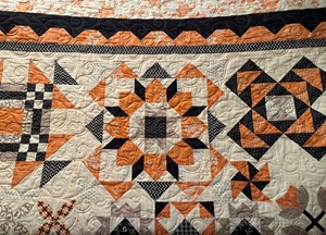 a beautiful orange, black and beige quilt with longarm work by Red Bridge Quilts