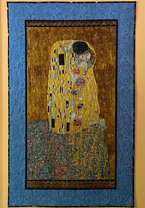 A quilted wall hanging of Klimt's "The Kiss" with a blue border