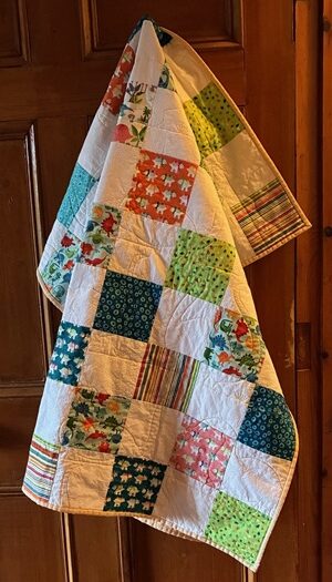 a patchwork quilt with lots of colourful blocks featuring all sorts of dinosaurs, quilted dinosaurs in medium yellow thread cover the quilt