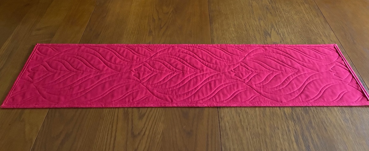 the back side of a beautiful quilted table runner in Christmas red with six lovely images on the front