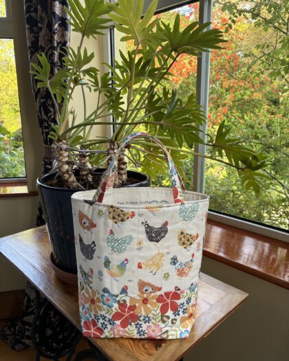 colourful and cheery tote bag with a hen theme next to a large-lobed plant on a small table