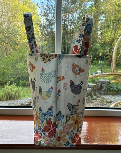 Fabric tote bag with two fabric handles featuring a colorful chicken and floral pattern on a windowsill.