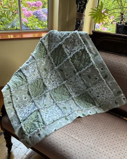 Patchwork quilt draped over a sofa in a sunlit living room; pastel blue-green squares with frayed seams.