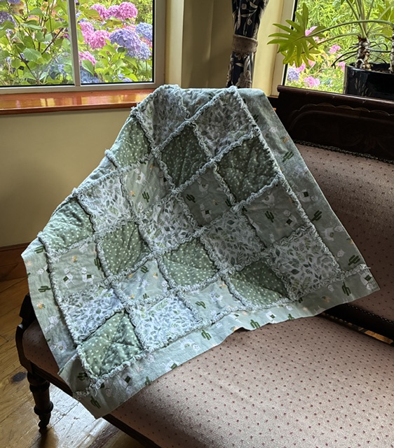 Patchwork quilt draped over a sofa in a sunlit living room; pastel blue-green squares with frayed seams.