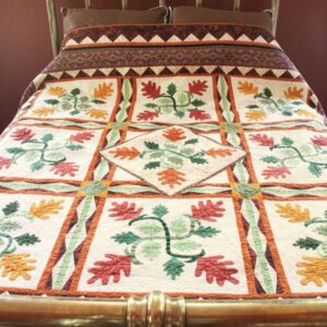 An oak leaf quilt on a double bed with red and gold leaves in each block and a central leaf emblem in green in each block