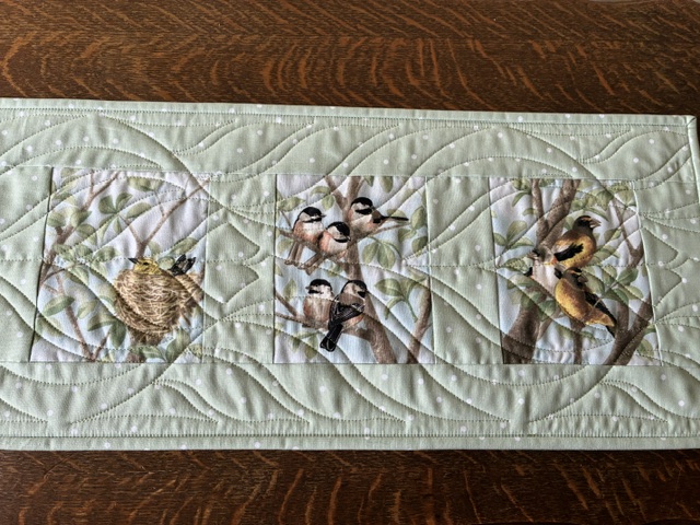 Quilted fabric border with three square panels: a bird nest in a circle, a group of small birds on a branch, and a single bird perched on a branch.