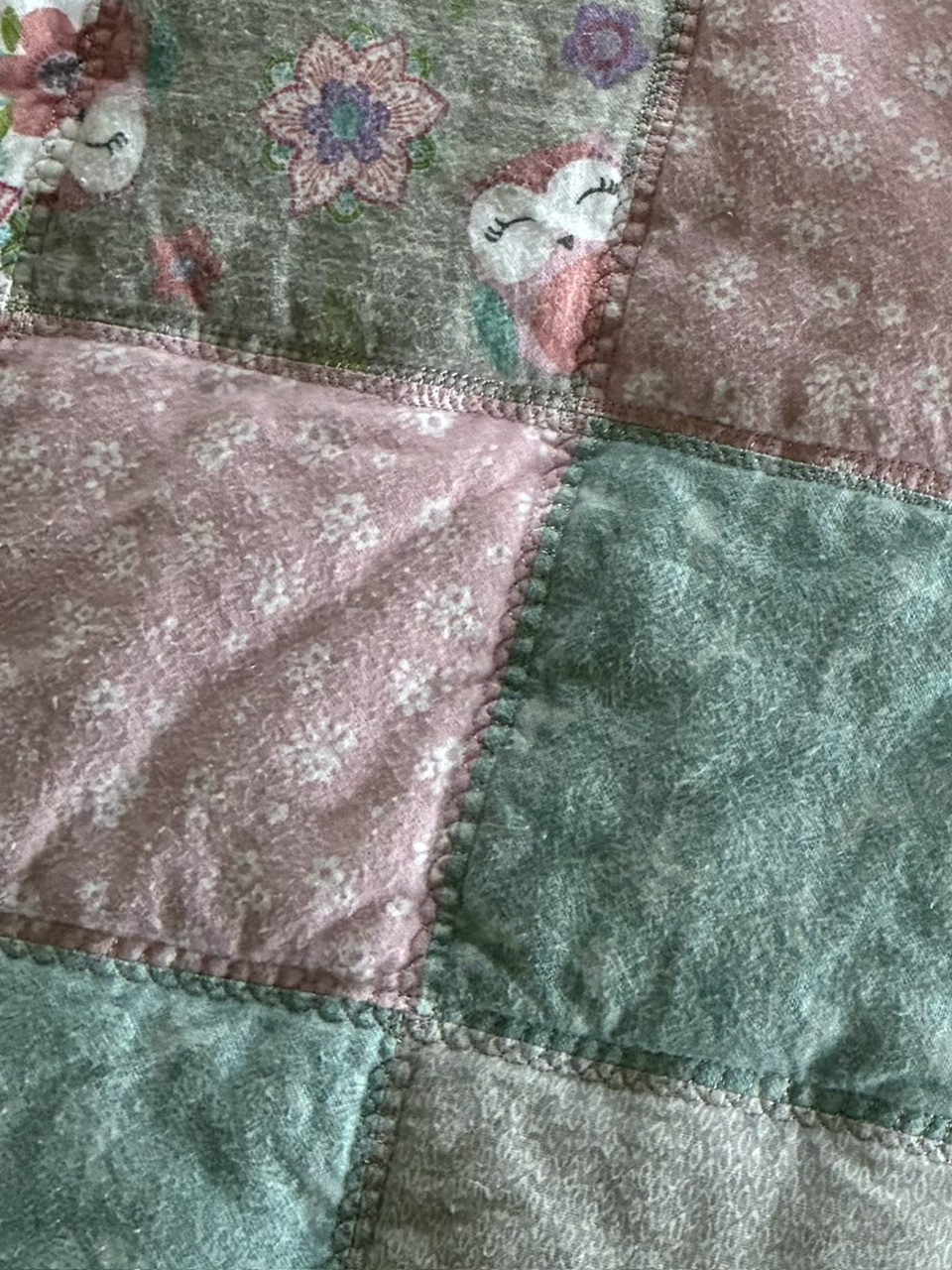 Quilted patchwork fabric with teal, pink, and gray squares, stitched together with visible seam lines and floral patterns in some blocks.