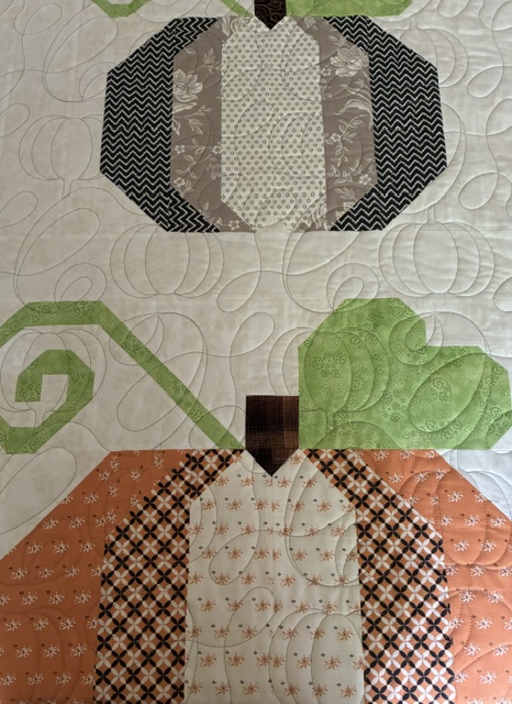 Sample of pieced pumpkins on a quilt top with a pattern of loops and pumpkins quilted all over with a longarm machine