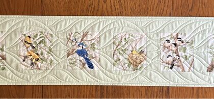 Long quilted table runner with six bird images quilted with a bird feather design.
