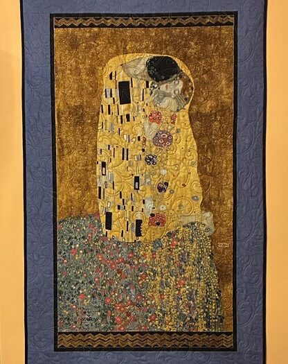Quilted wall hanging recreating Klimt's The Kiss: gold-clad couple embracing on a patterned, glittering background with a blue outer frame.