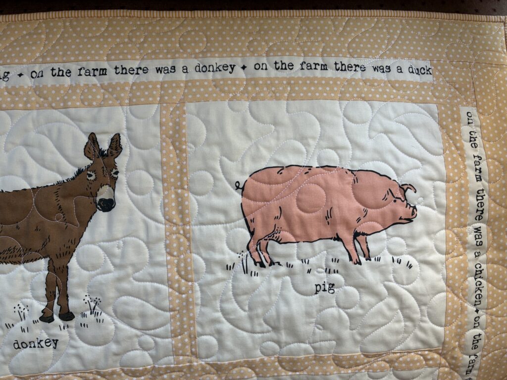 Patchwork quilt panel with a brown donkey on the left and a pink pig on the right, bordered by beige polka dots.