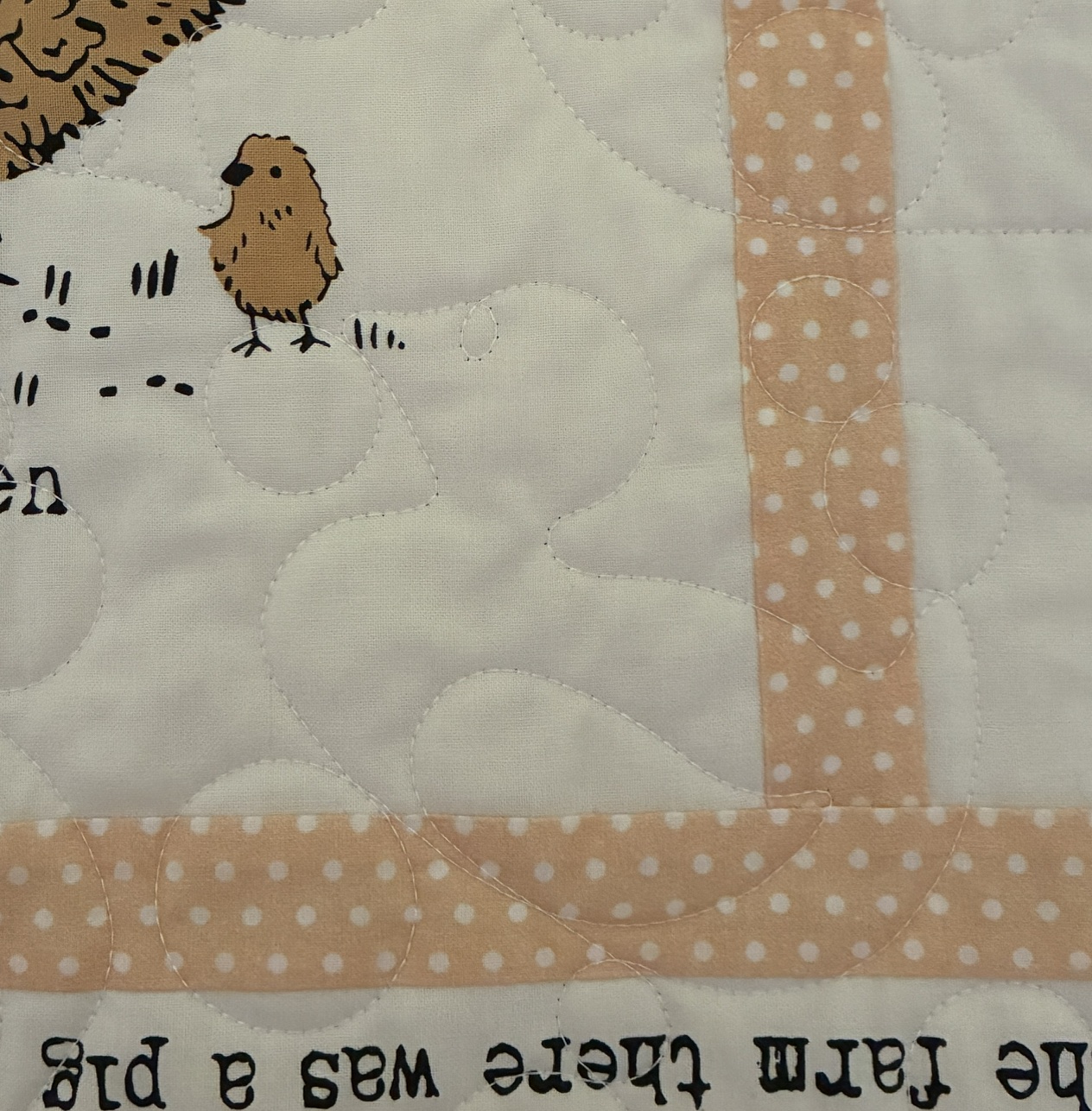 Close-up of a quilt block with peach polka-dot strips and a small brown chick illustration on light fabric.