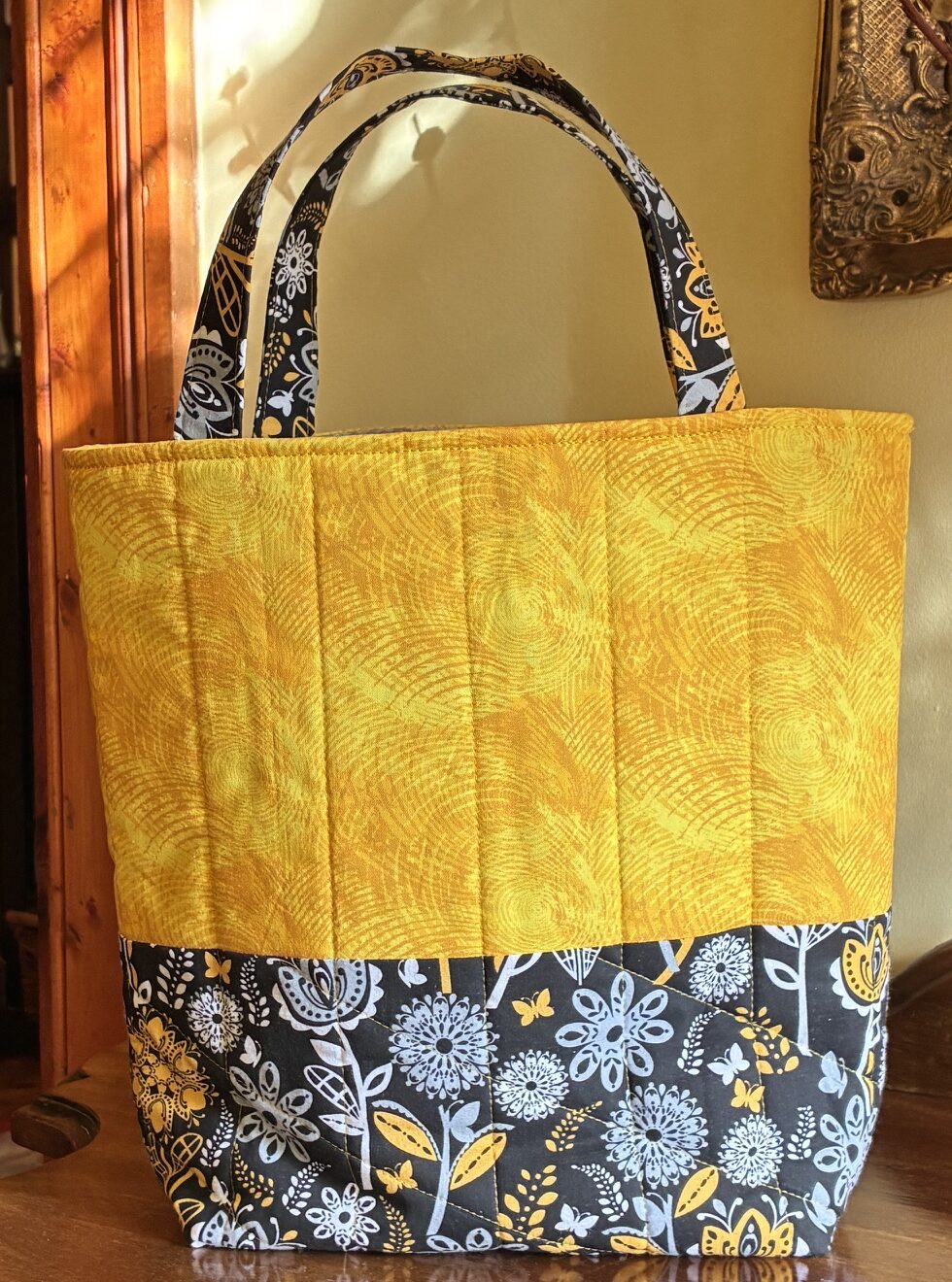 A cotton tote bag with a bright yellow top section combined with a black, yellow and white paisley lower section and matching handles
