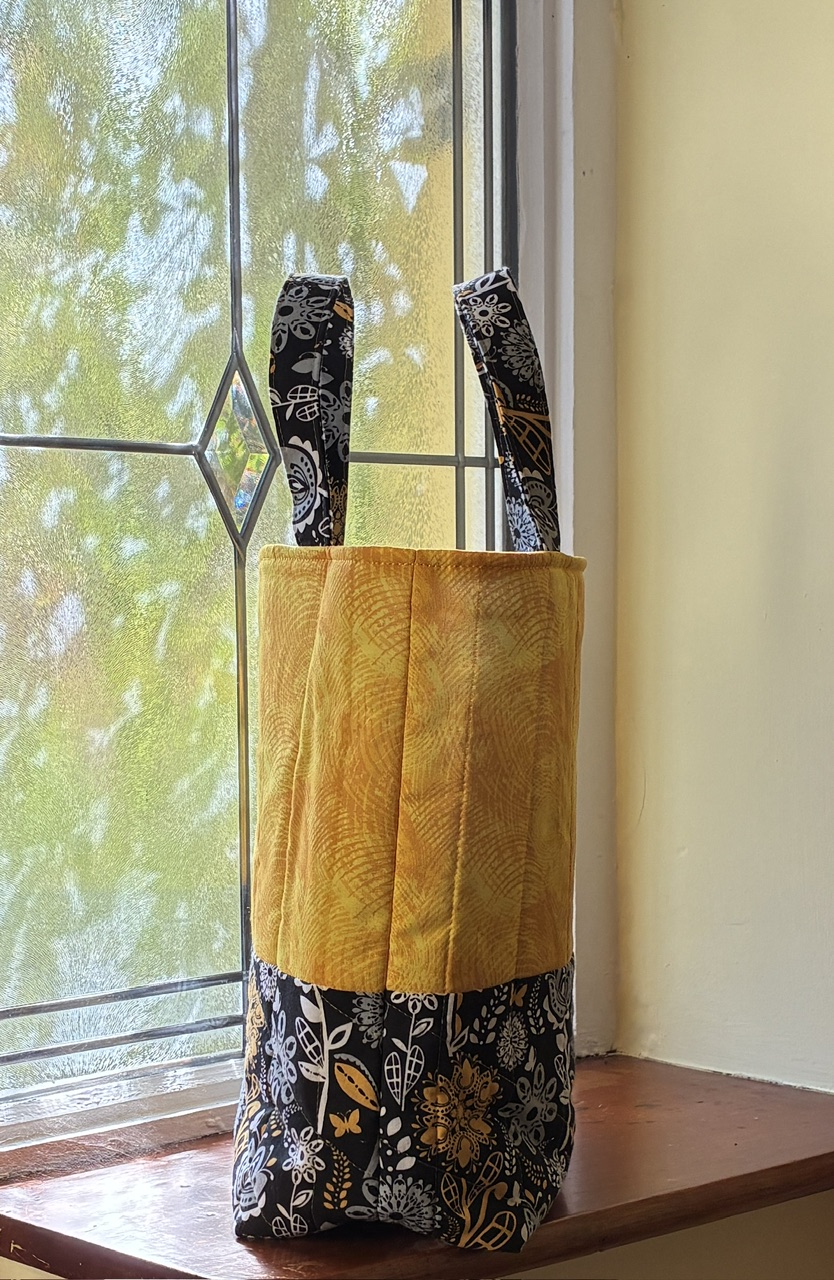 A yellow, black and white tote bag on a window ledge viewed from the side