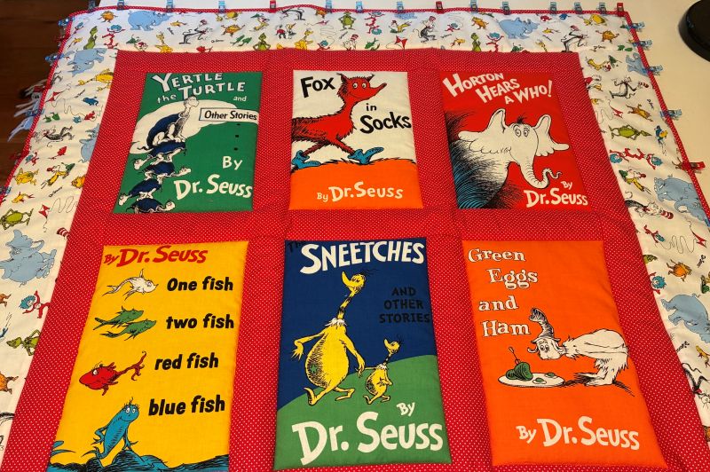 An image of a child's quilt featuring Dr. Seuss book covers with borders all around and clips holding the binding in place for stitching