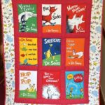 A colourful quilt featuring images of books by Dr. Seuss with red and white polka dot sashing and a border with Dr. Seuss characters